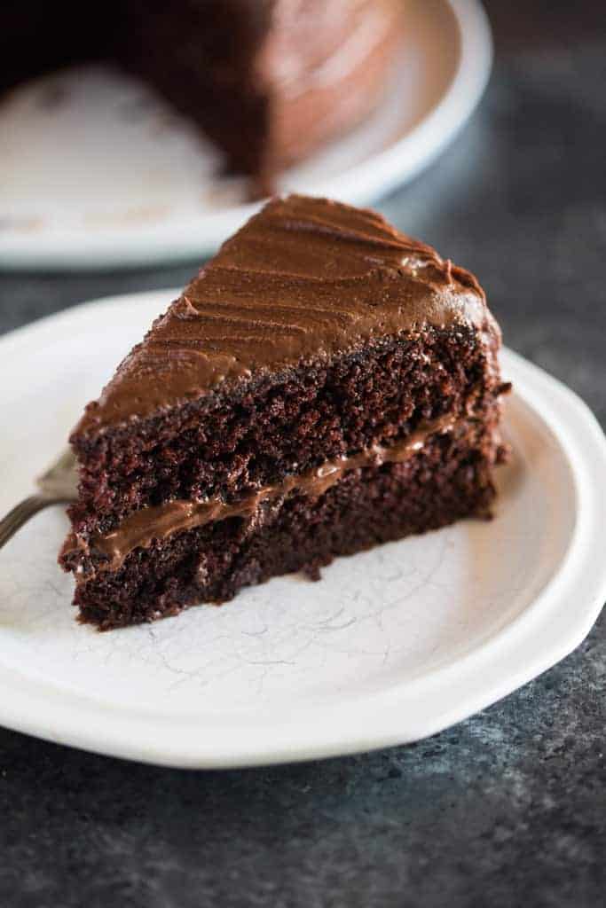 A slice of Hershey's perfectly chocolate chocolate cake on a white plate with the whole cake in the background.