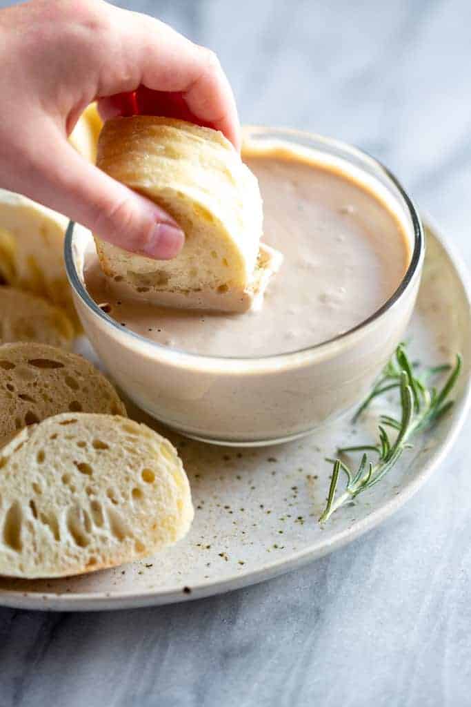 Hand dipping a piece of bread into dip.