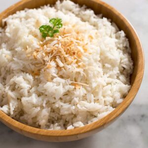 A wooden bowl filled with coconut rice with toasted coconut sprinkled on top.
