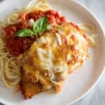 Chicken Parmesan served over spaghetti noodles with marinara sauce on a white plate, on a white marble board.