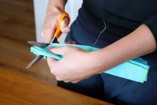 Hands holding tissue paper and scissors and making a cut into the tissue paper.