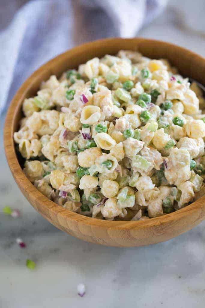 Tuna Pasta salad with peas, tuna, celery, onion and a mayo greek yogurt sauce, mixed together and served in a wood bowl.
