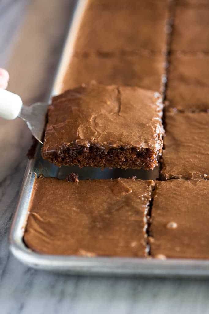 A slice of chocolate sheet cake being lifted out of a sheet pan with a spatula.