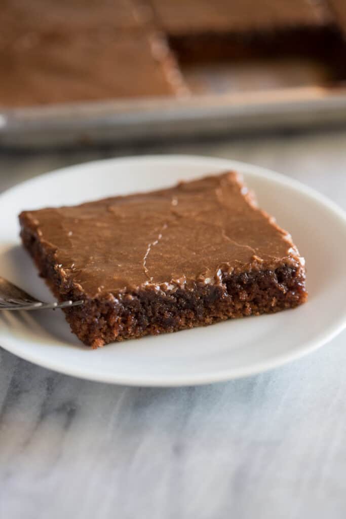 Square slice of Texas sheet cake on a small white plate with a fork.