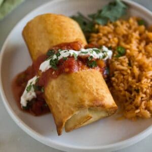 Chicken chimichanga topped with salsa, sour cream and chopped cilantro with a side of Mexican rice.