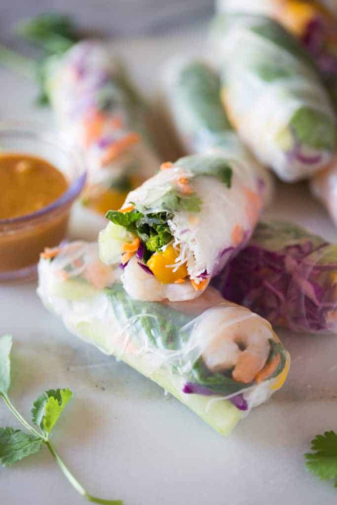 Fresh Spring rolls layered on top of each other, next to a bowl of peanut sauce for dipping.