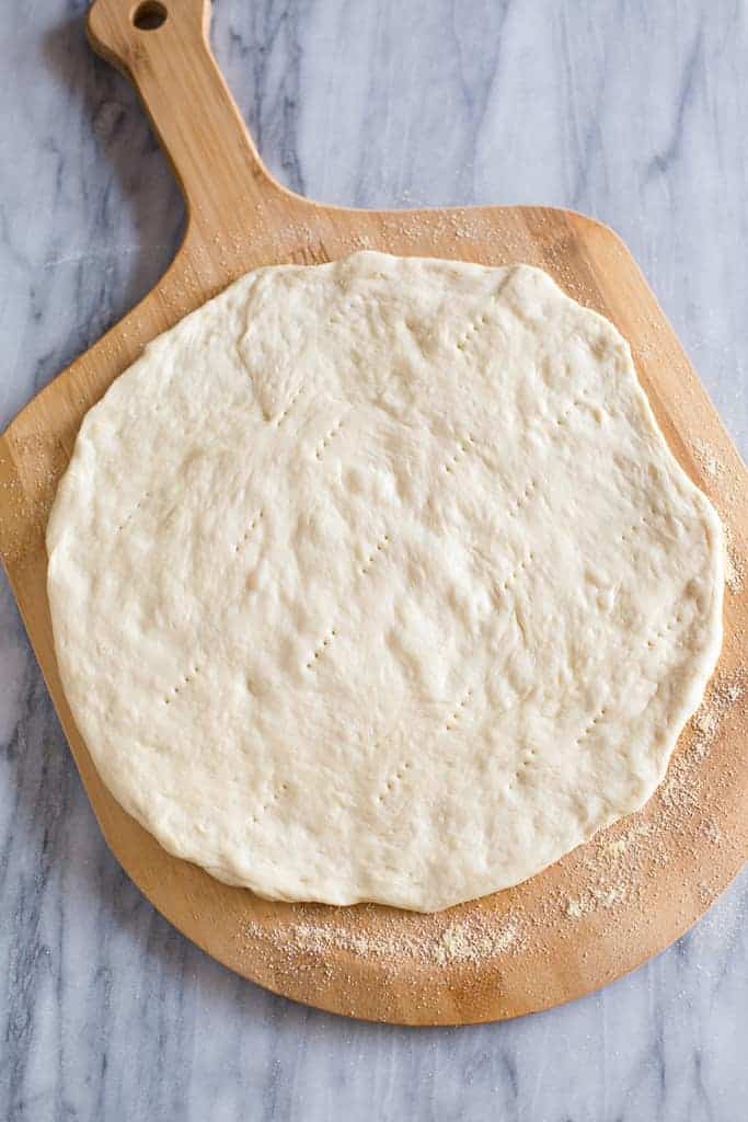 Pizza dough pressed into a circle on a wood pizza peel. 