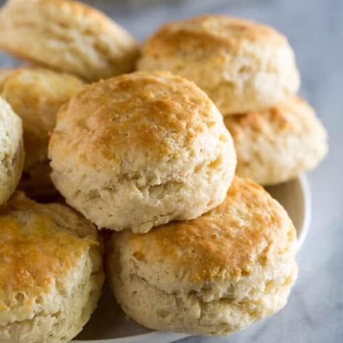 Buttermilk biscuits stacked on a white plate with butter in the background.