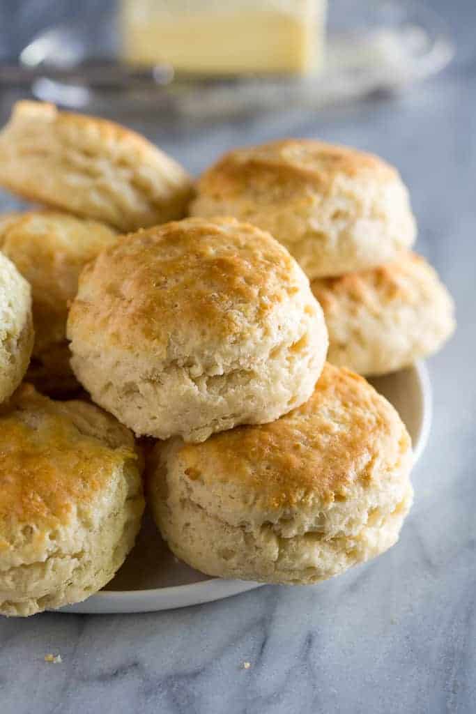 Buttermilk biscuits stacked on a white plate with butter in the background.
