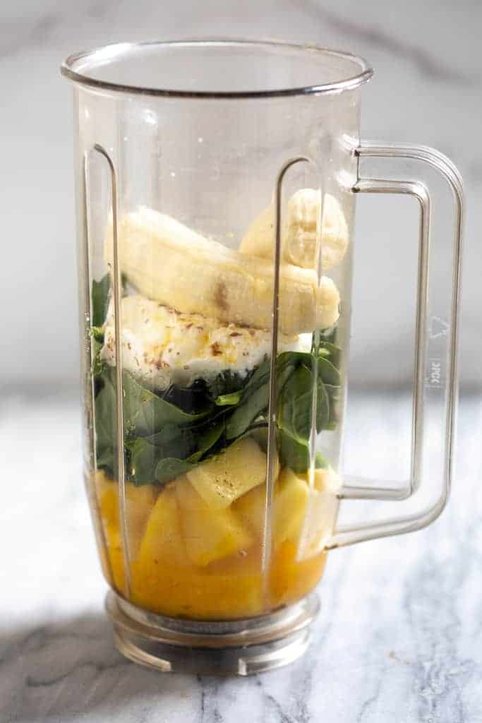 Blender with orange juice, spinach, pineapple, and bananas in it, ready to blend into a smoothie.