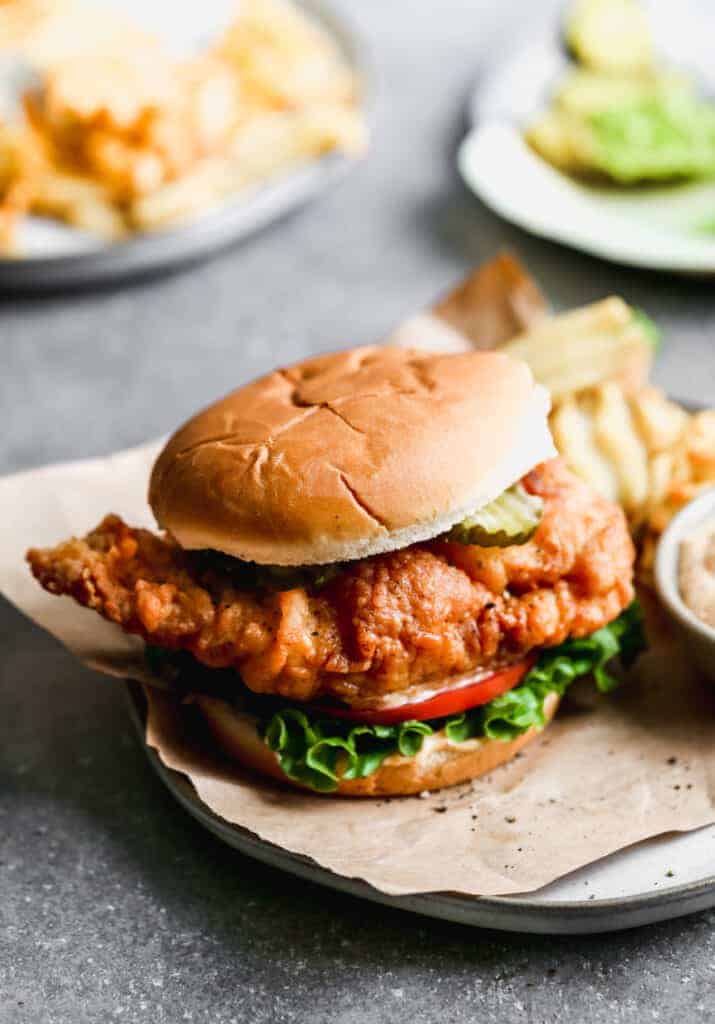 A copycat Chick-Fil-A chicken sandwich on a plate with fries and sauce.