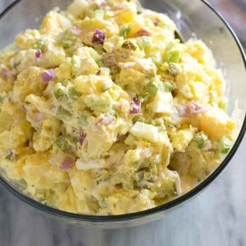 Potato salad served in a clear glass serving bowl with a spoon.