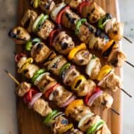 Six chicken kebabs on bamboo skewers with bell pepper and onion, served on a wood board.