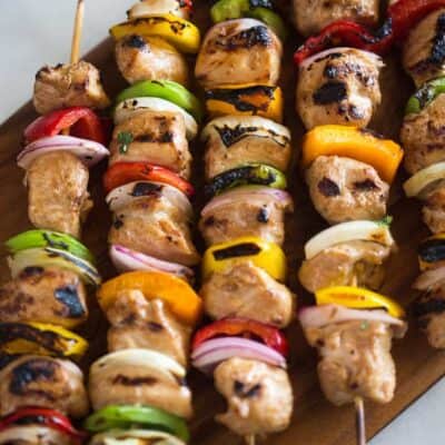Chicken kebabs on bamboo skewers with yellow, red, and green bell pepper chunks and purple onion.