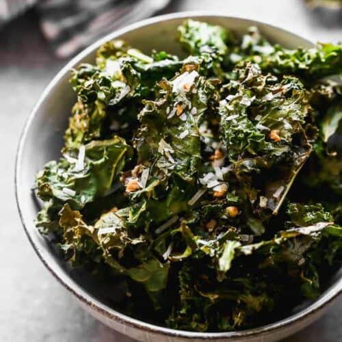 Kale chips in a bowl with a hand towel in the background.
