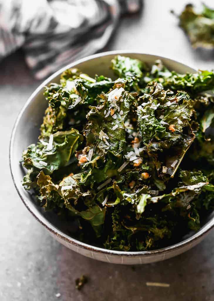 Kale chips in a bowl with a hand towel in the background.