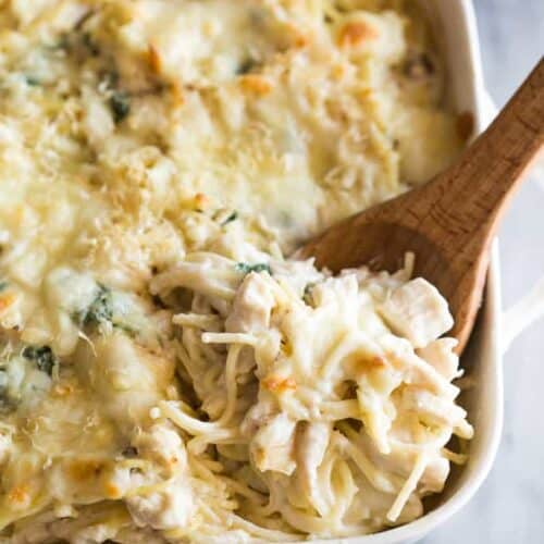 Chicken tetrazzini baked in a white casserole dish with a wooden spoon about to scoop out a serving.