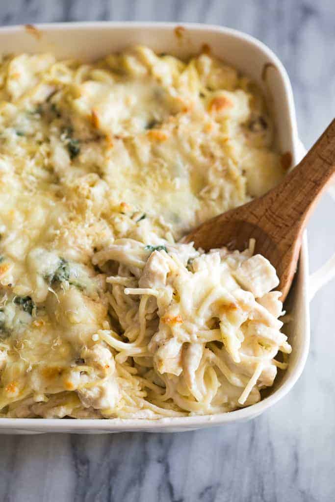 Chicken tetrazzini baked in a white casserole dish with a wooden spoon about to scoop out a serving.