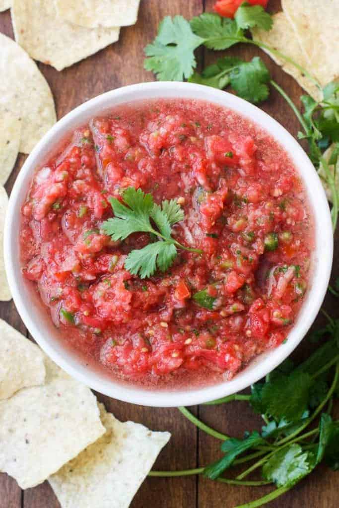 Fresh homemade salsa served in a white bowl made with roma tomatoes, cilantro, onion, serrano peppers, garlic and salt.