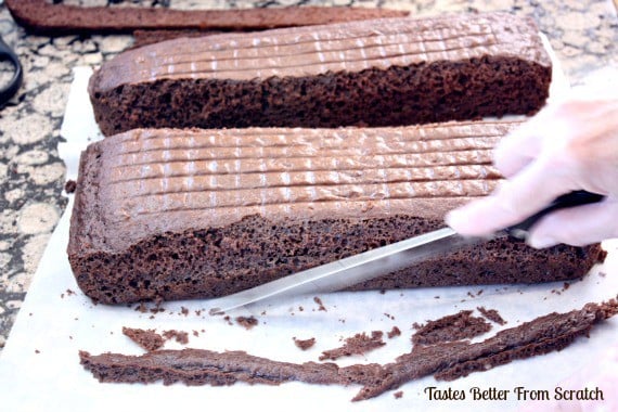 A baked cake being cut into patterns for an airplane cake.