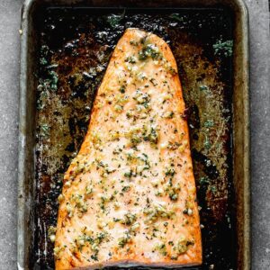 A filet of salmon baked on a baking sheet, topped with a lemon garlic sauce.