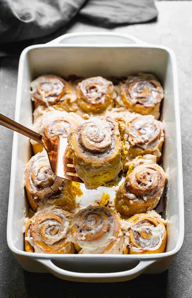 A spatula lifting out a cinnamon roll from a pan.