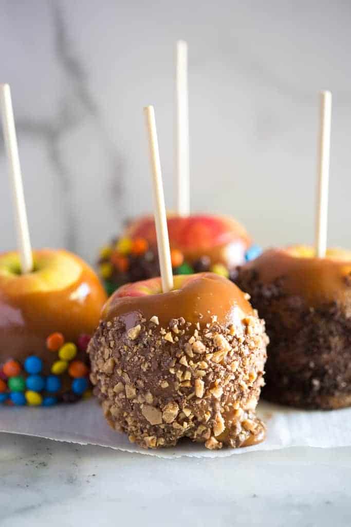 Four caramel apples with different toppings included crushed toffee bits, crushed Oreos and mini m&m candies.