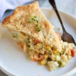 A slice of chicken pot pie with homemade crust and filling with vegetables and chicken, served on a white plate with a fork.