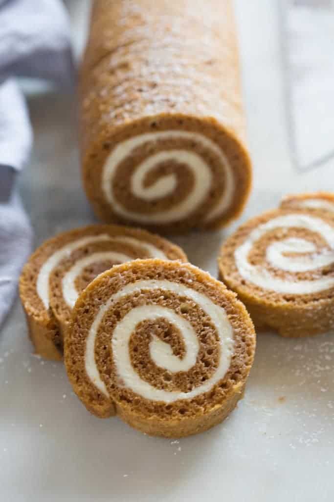 A pumpkin roll laying vertically with four slices of pumpkin roll laying in front of it.