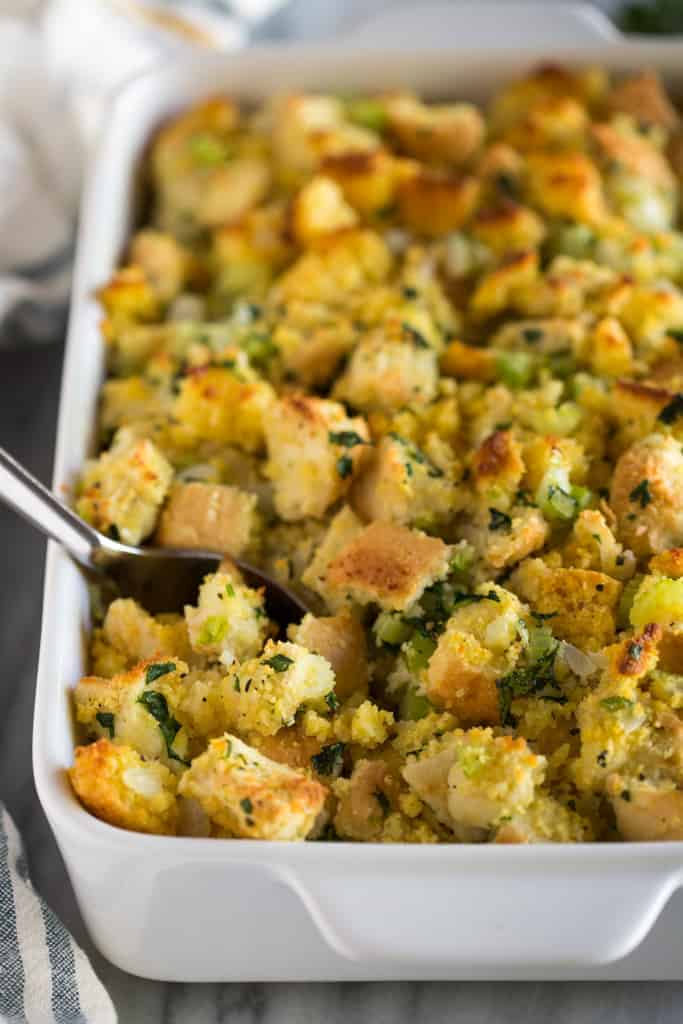 A close up photo of a pan of cornbread stuffing with a spoon in it for serving.