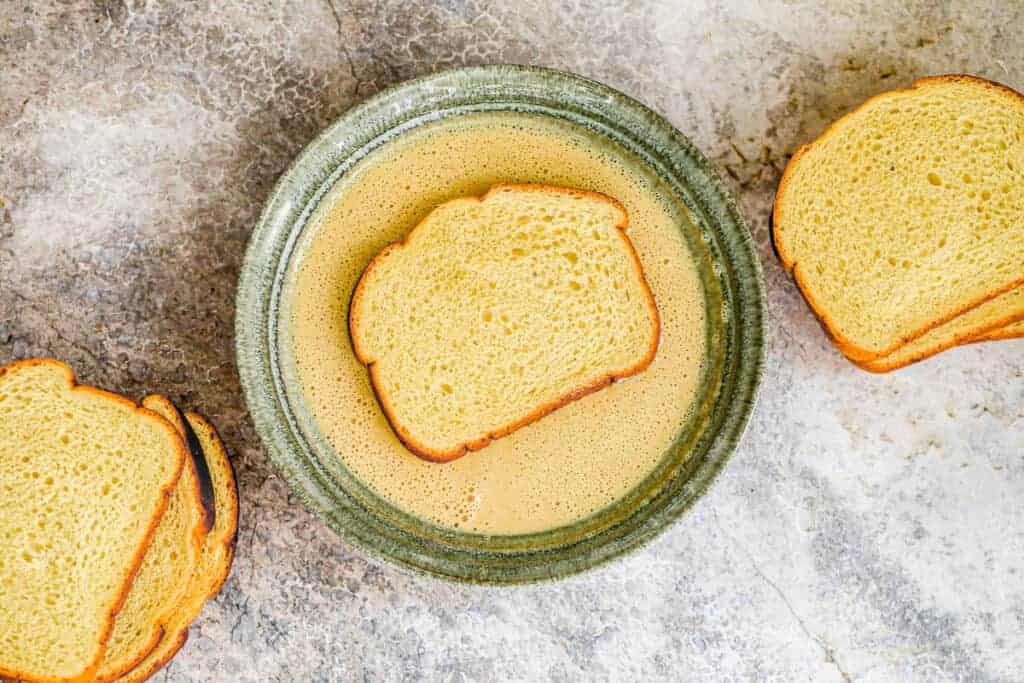 Bread laid on top of french toast batter in a shallow bowl.
