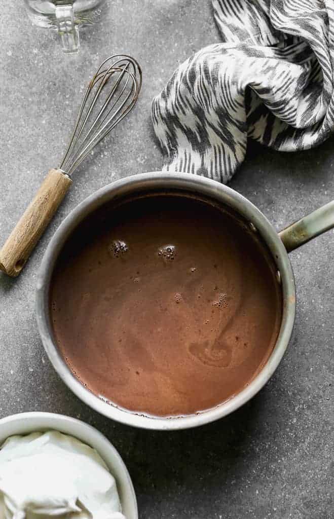 A saucepan with homemade hot cocoa and a whisk and hand towel on the side.