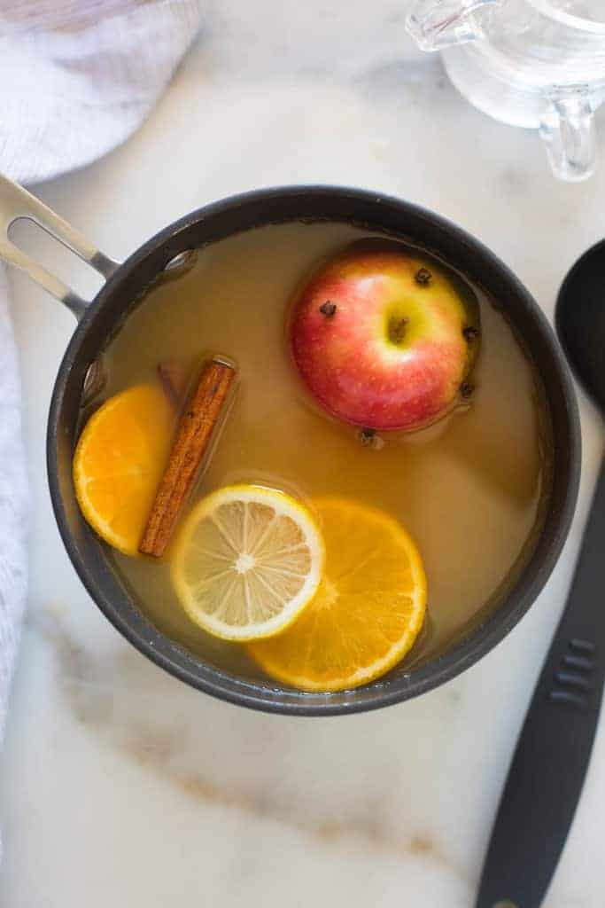 An overhead view of a large pot filled with wassail, orange slices, and apple, and cinnamon sticks.