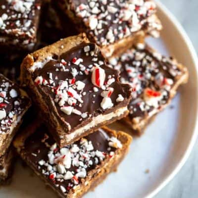 Peppermint Brownie squares with chocolate frosting and crushed candy canes on a white plate.