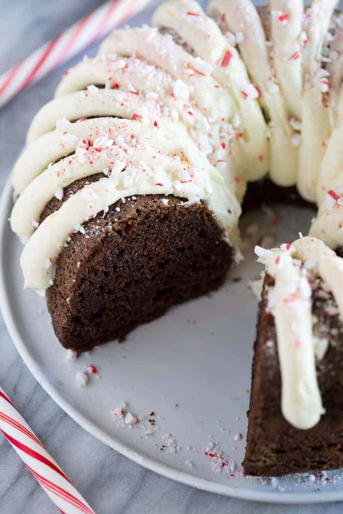A chocolate bundt cake with cream cheese frosting on a white plate, with a slice removed.