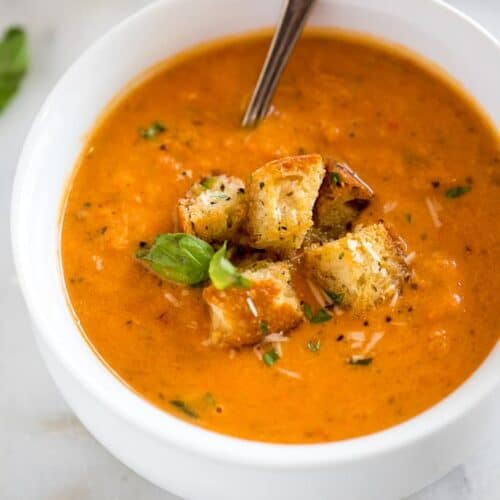 Creamy tomato basil soup in a white soup bowl topped with croutons and a spoon inside the bowl.