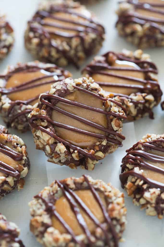 Many Turtle Thumbprint cookies on a baking sheet, each one has a caramel filling and chocolate drizzled on top.