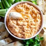 A bowl of buffalo chicken dip with bread slices, celery and chips around it.