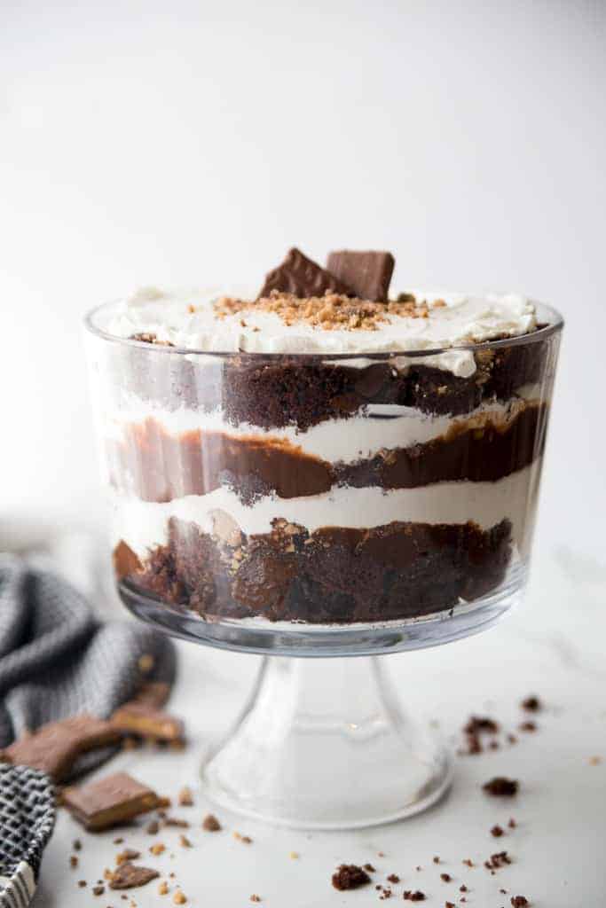 Chocolate trifle made with chocolate cake, whipped cream, chocolate pudding and heath candy, with a dish towel and crushed heath to the side.