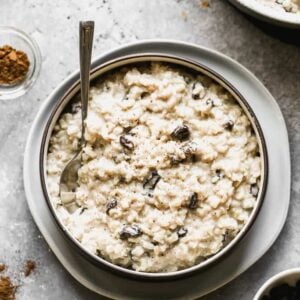 A bowl of homemade brown rice pudding with raisins, and a spoon in it.