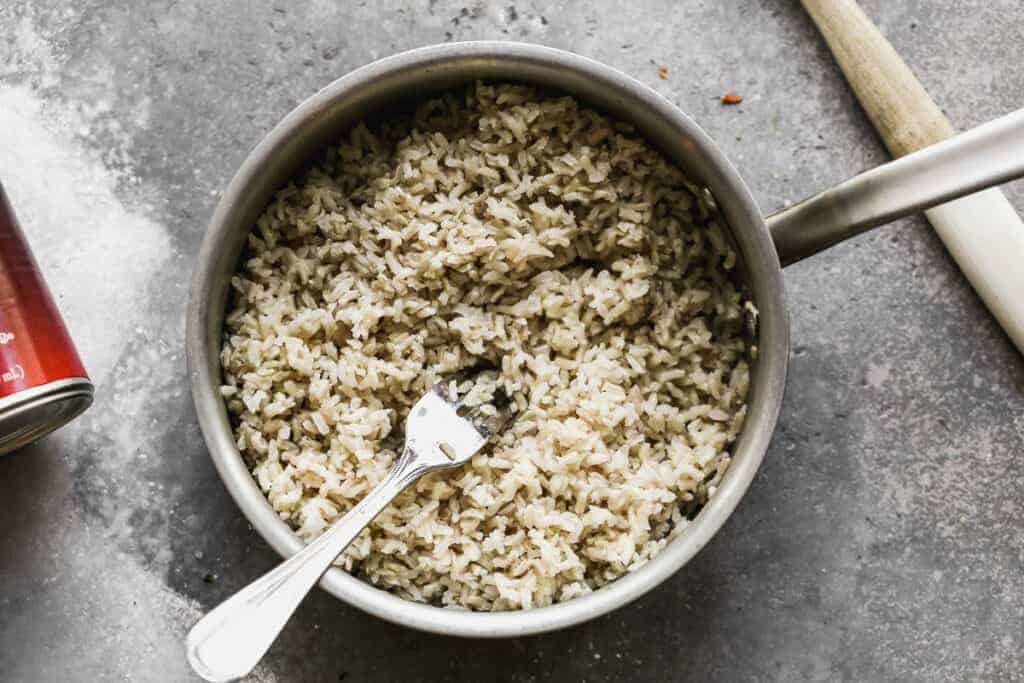 A pot of cooked brown rice being fluffed with a fork.