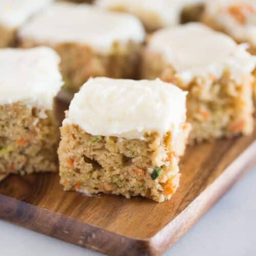 Carrot and zucchini bars with lemon cream cheese frosting on a wood cutting board.
