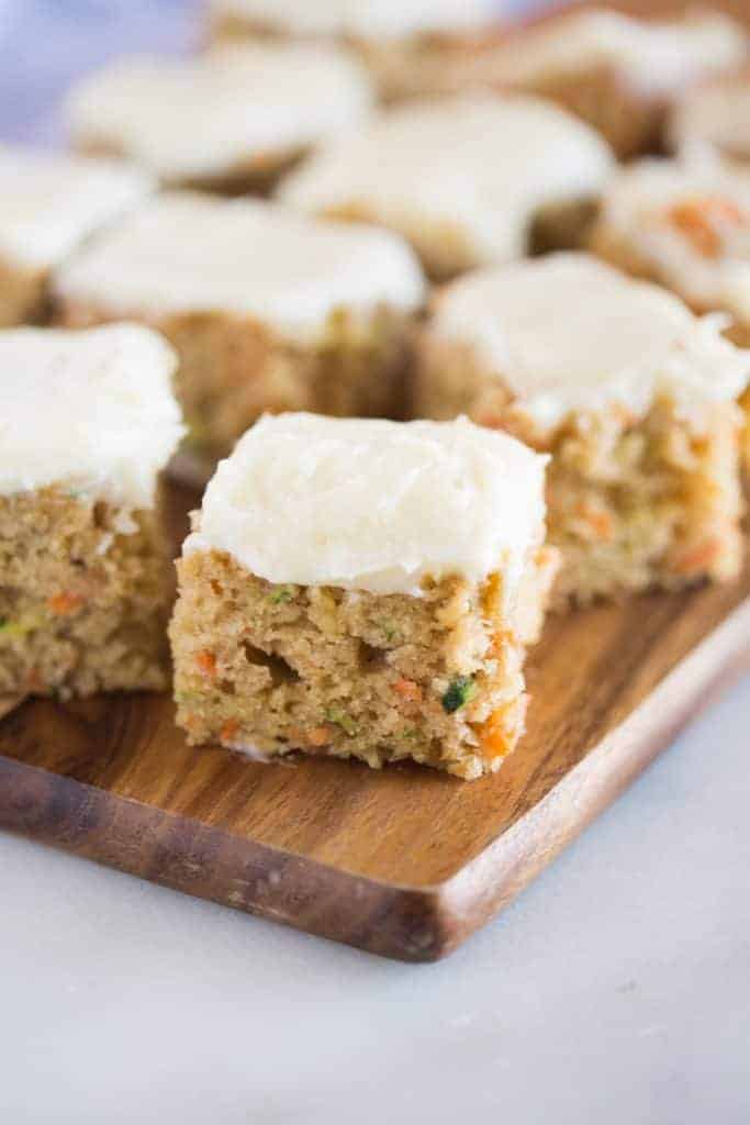 Carrot and zucchini bars with lemon cream cheese frosting on a wood cutting board.