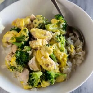 Chicken divan made with rice, chicken, broccoli and sauce served in a white bowl with a spoon.