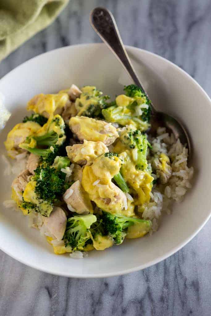 Chicken divan made with rice, chicken, broccoli and sauce served in a white bowl with a spoon.