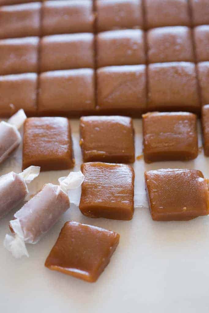 Homemade caramels cut into squares, with three wrapped in wax paper.