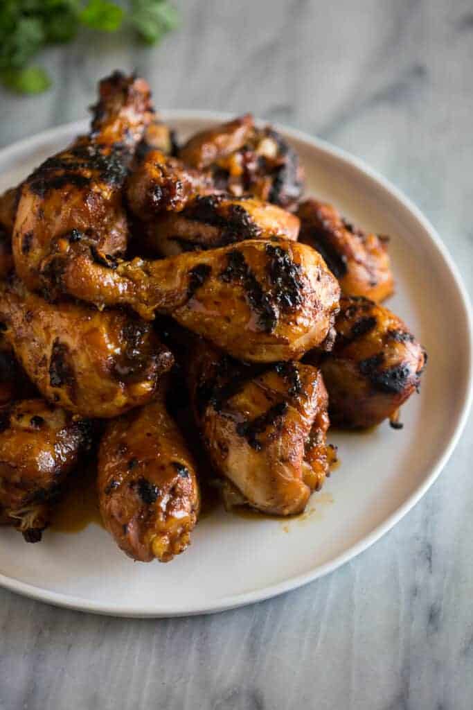 BBQ chicken drumsticks stacked into a pile on a white plate.