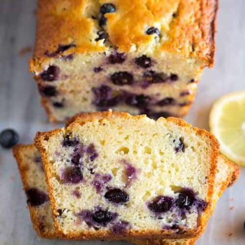 Stacked slices of lemon blueberry bread with the loaf of quick bread behind it.