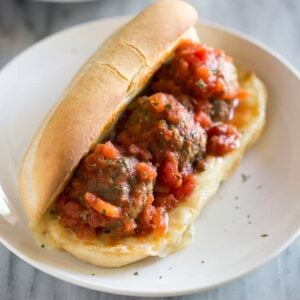 Meatball sub on a toasted hoagie with three meatballs and sauce, on a white plate.