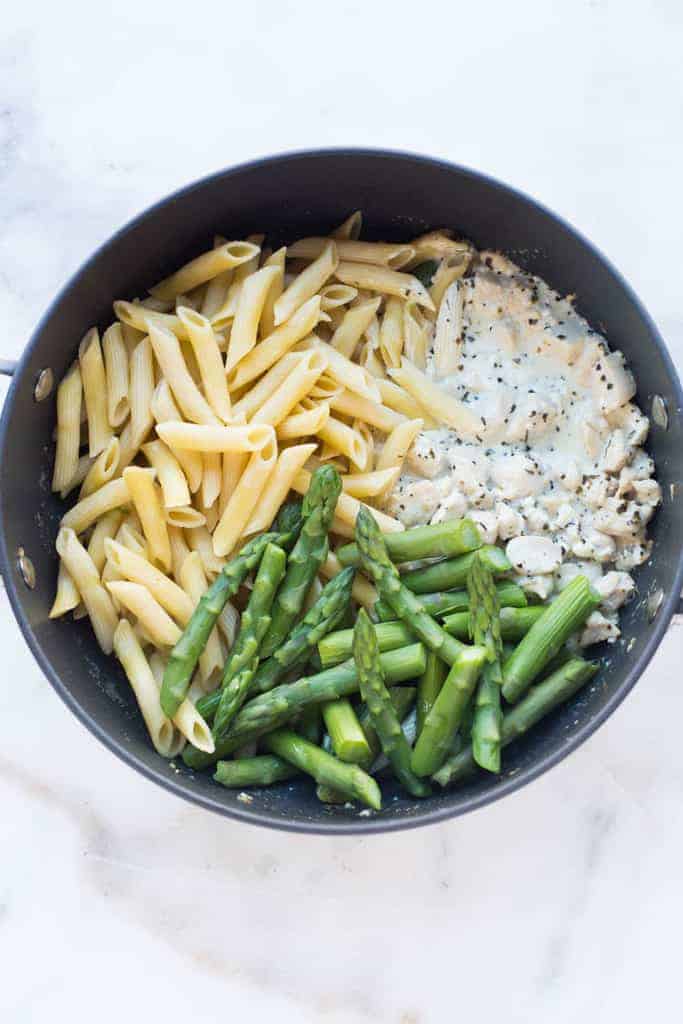 Skillet with the ingredients to toss together creamy chicken and asparagus penne noodles, asparagus and creamy white sauce